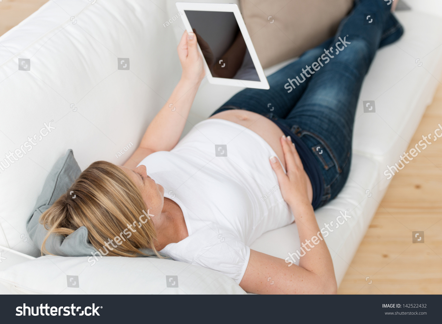 stock-photo-young-pregnant-woman-reading-ebook-on-digital-tablet-while-lying-on-sofa-at-home-142522432